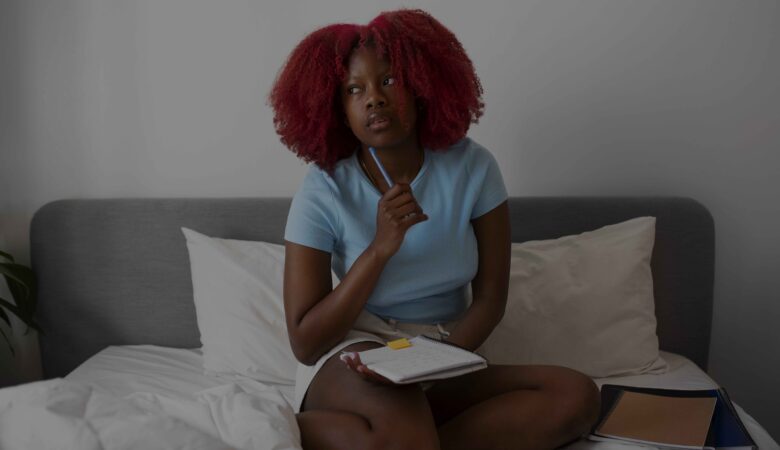 portrait of a woman sitting on her pen holding a jotter and pen in a thinking and studying mode